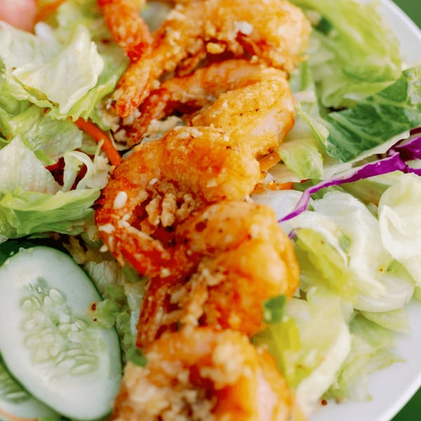 Crispy fried shrimp with sesame seeds on a bed of fresh green lettuce and cucumber slices.