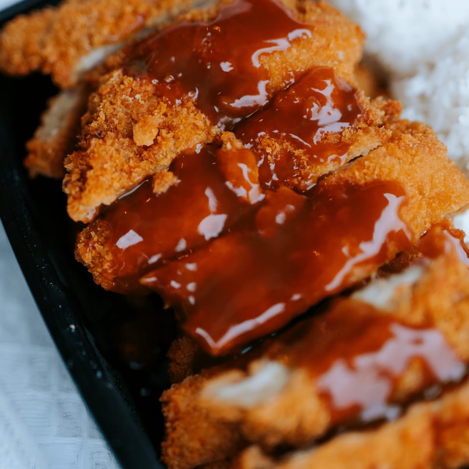 Close-up of L&L Hawaiian Barbecue's chicken katsu, drizzled with sauce and served with white rice.