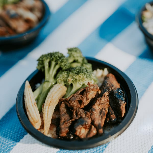 L&L Hawaiian Barbecue plate lunch with grilled meat, baby corn, and broccoli on a striped mat.