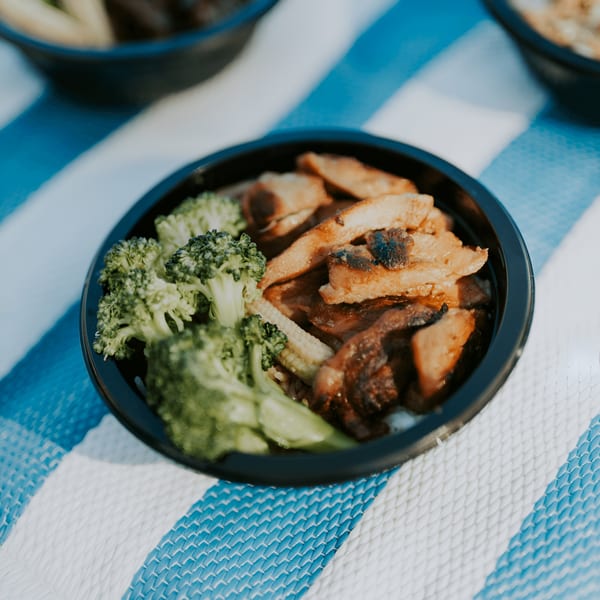 L&L Hawaiian Barbecue plate lunch with chicken, broccoli, and baby corn on a blue and white striped mat.